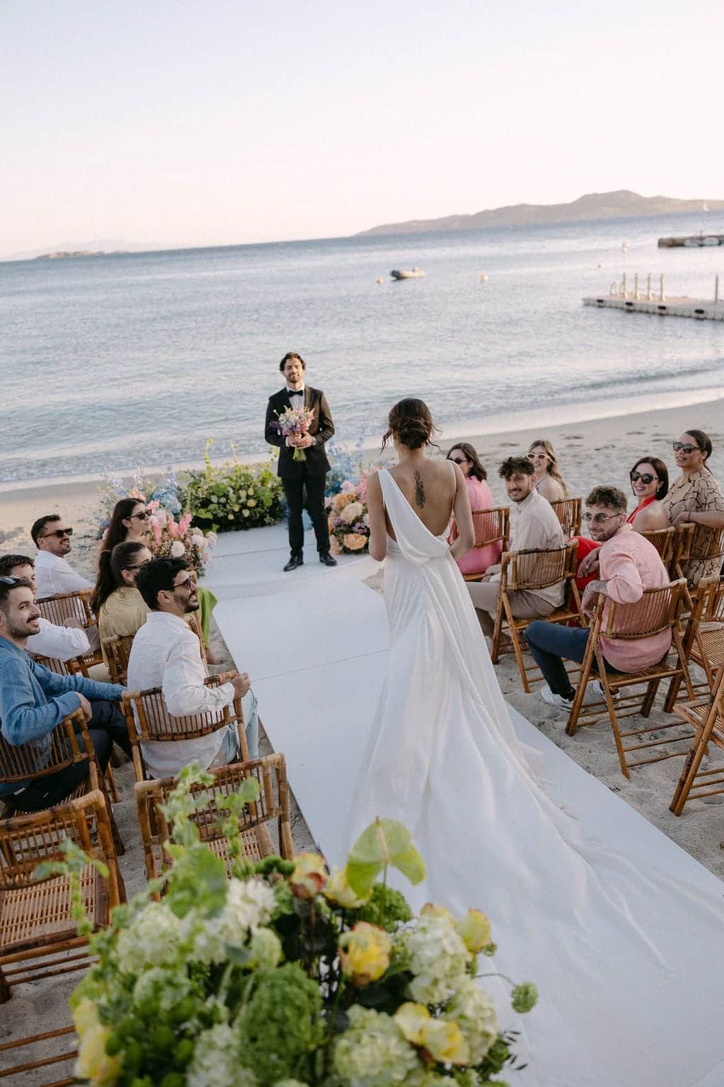 Bride walking down a beach aisle towards the groom as seated guests look on