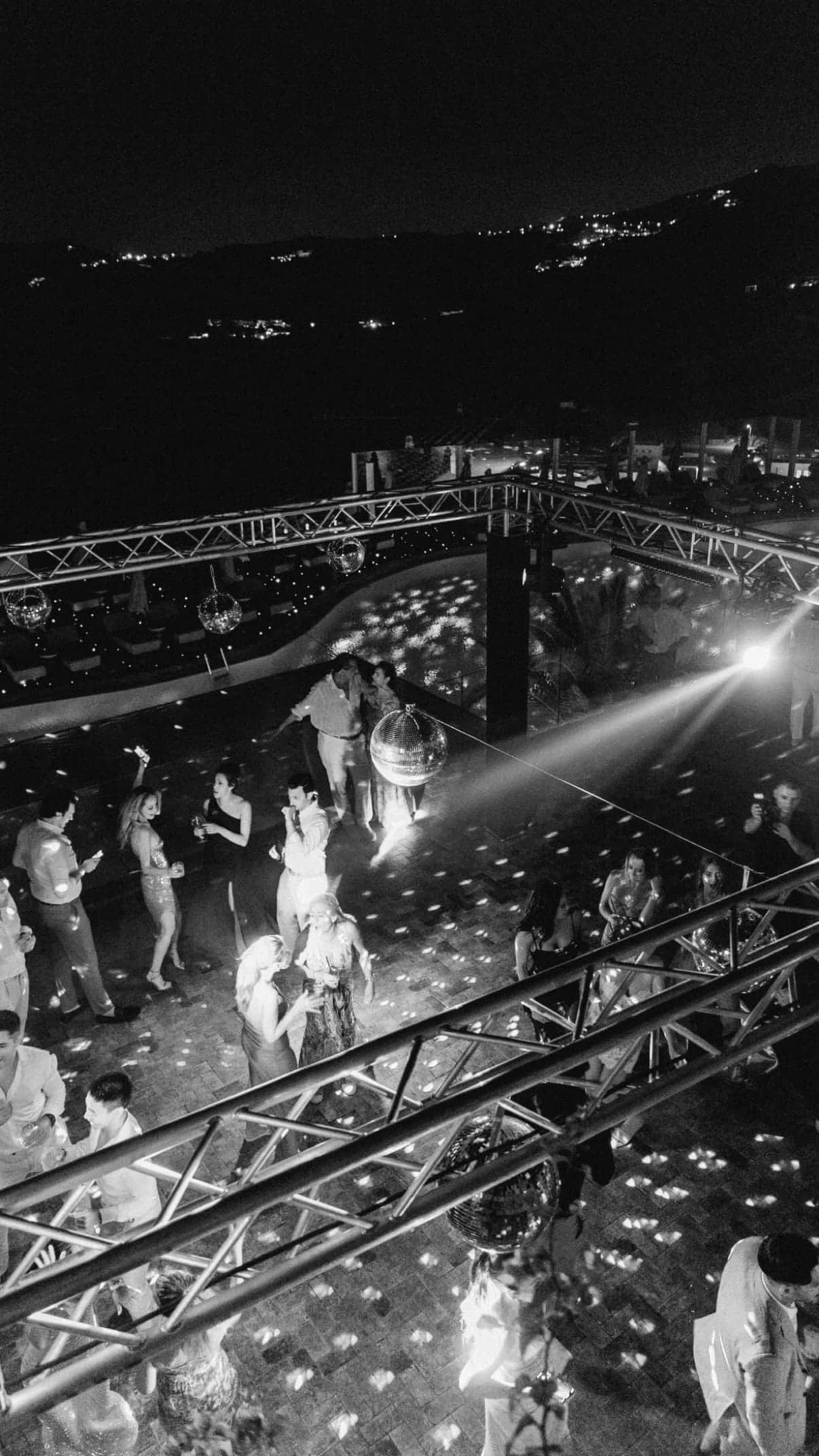 Black-and-white aerial view of a packed dance floor under a lighting truss with moving-head beams