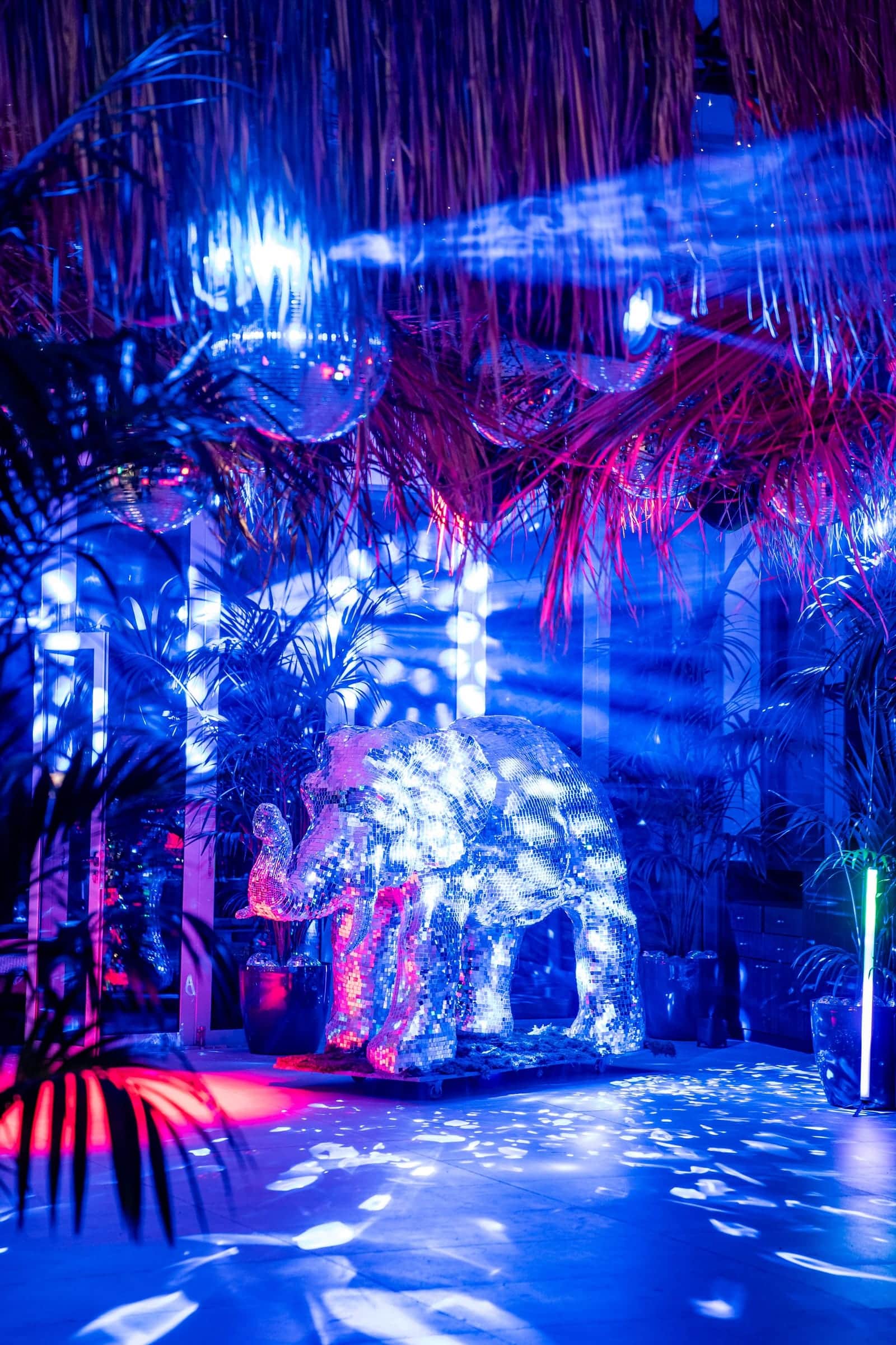 Mirror-ball elephant lit by blue beams and pink washes on a party dance floor