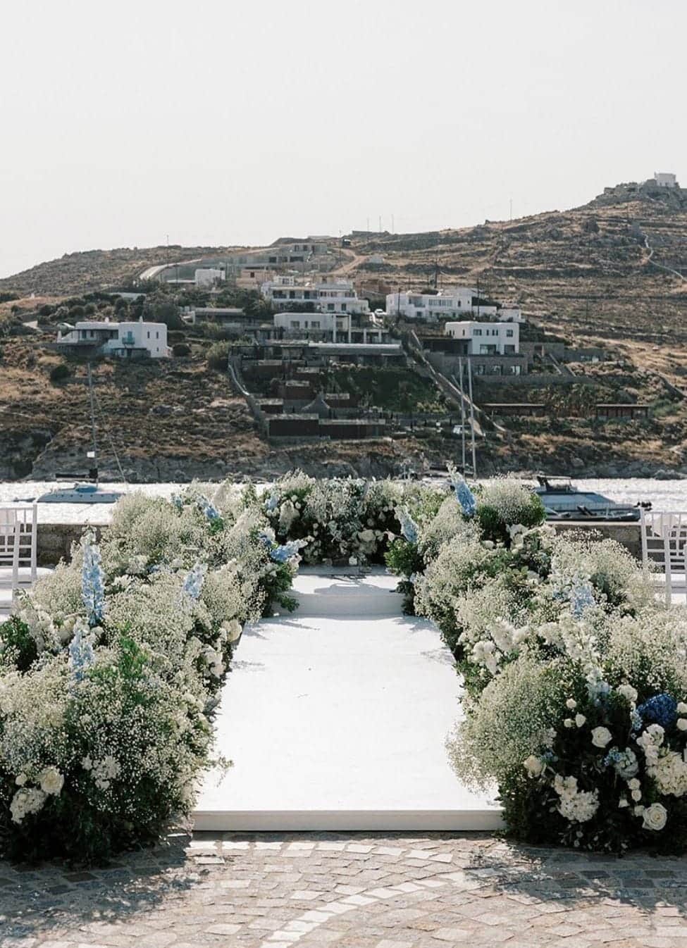 Wedding ceremony aisle lined with white flowers on a terrace overlooking the hills