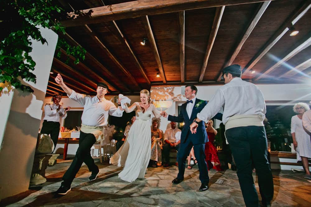 Bride and groom joining a traditional Greek dance with dancers in costume on a Mykonos terrace