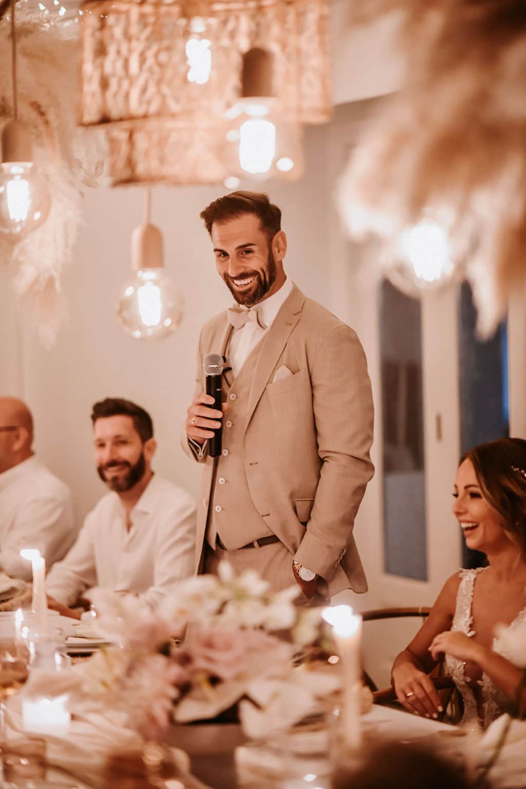 Groom giving a speech on a microphone at a candlelit wedding dinner