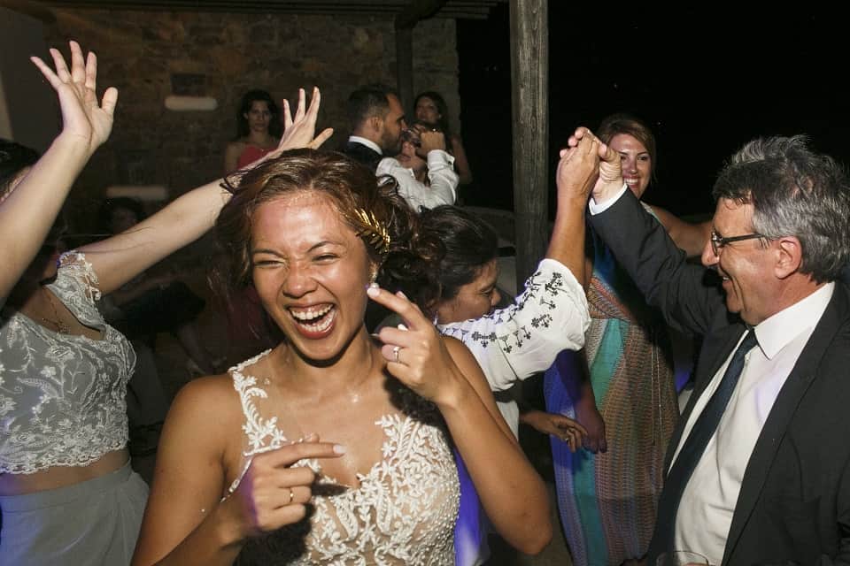 Bride laughing on the dance floor surrounded by guests at Jelly and Kostas's wedding