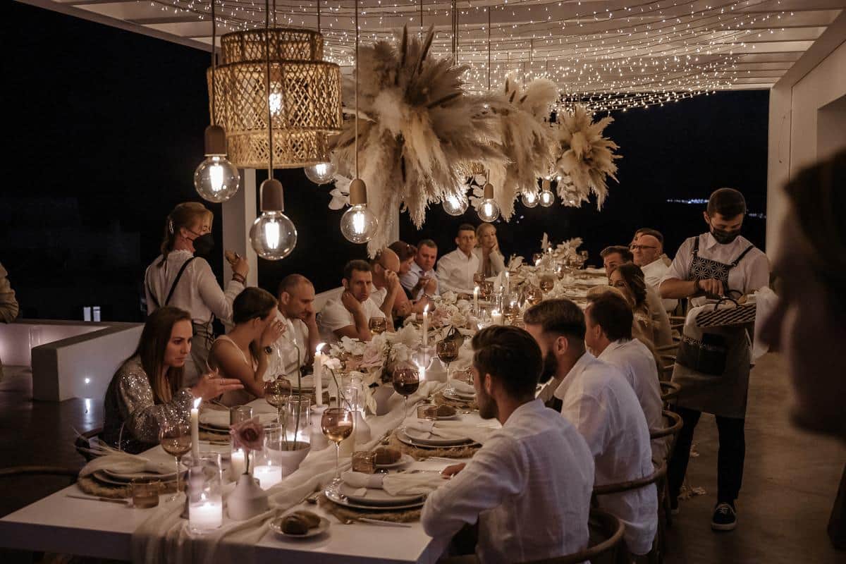 Guests at a long candlelit dinner table under pampas-grass chandeliers at Pascal and Désirée's wedding