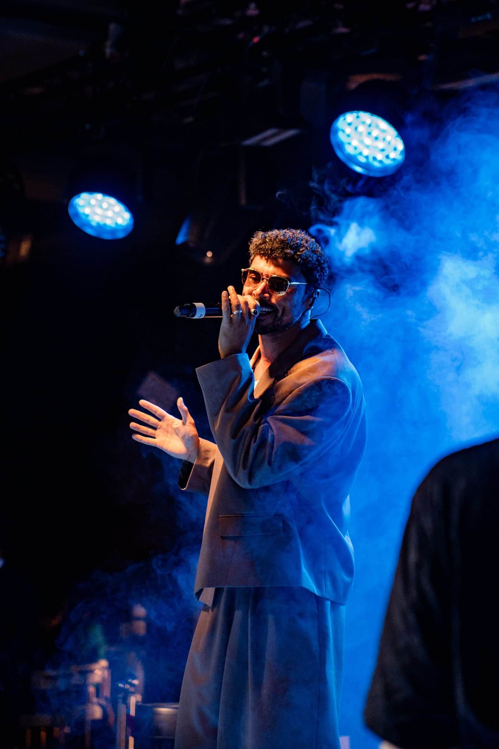 Performer singing into a microphone through blue haze and moving-head beams