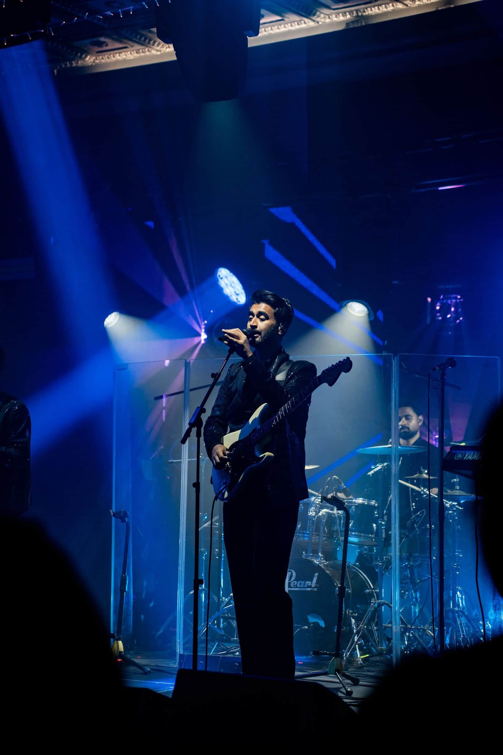 Singer with an acoustic guitar performing on stage under blue stage lighting