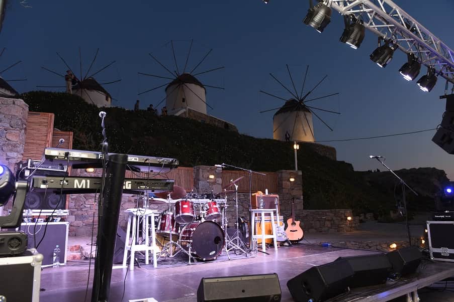 Concert stage with lighting truss and backline set up beneath the windmills of Mykonos at dusk