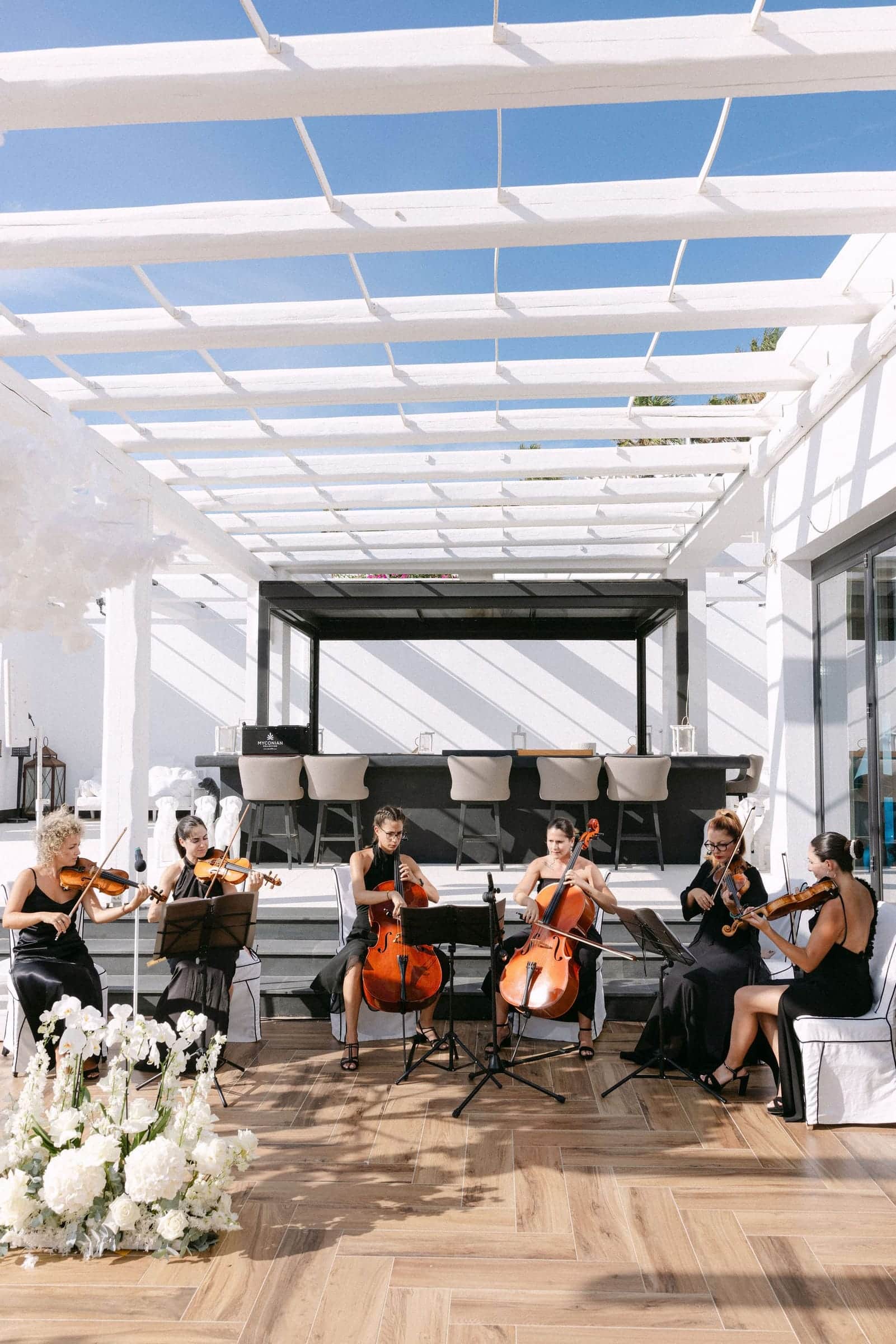 String ensemble of violins and cellos playing under a white pergola decorated with flowers