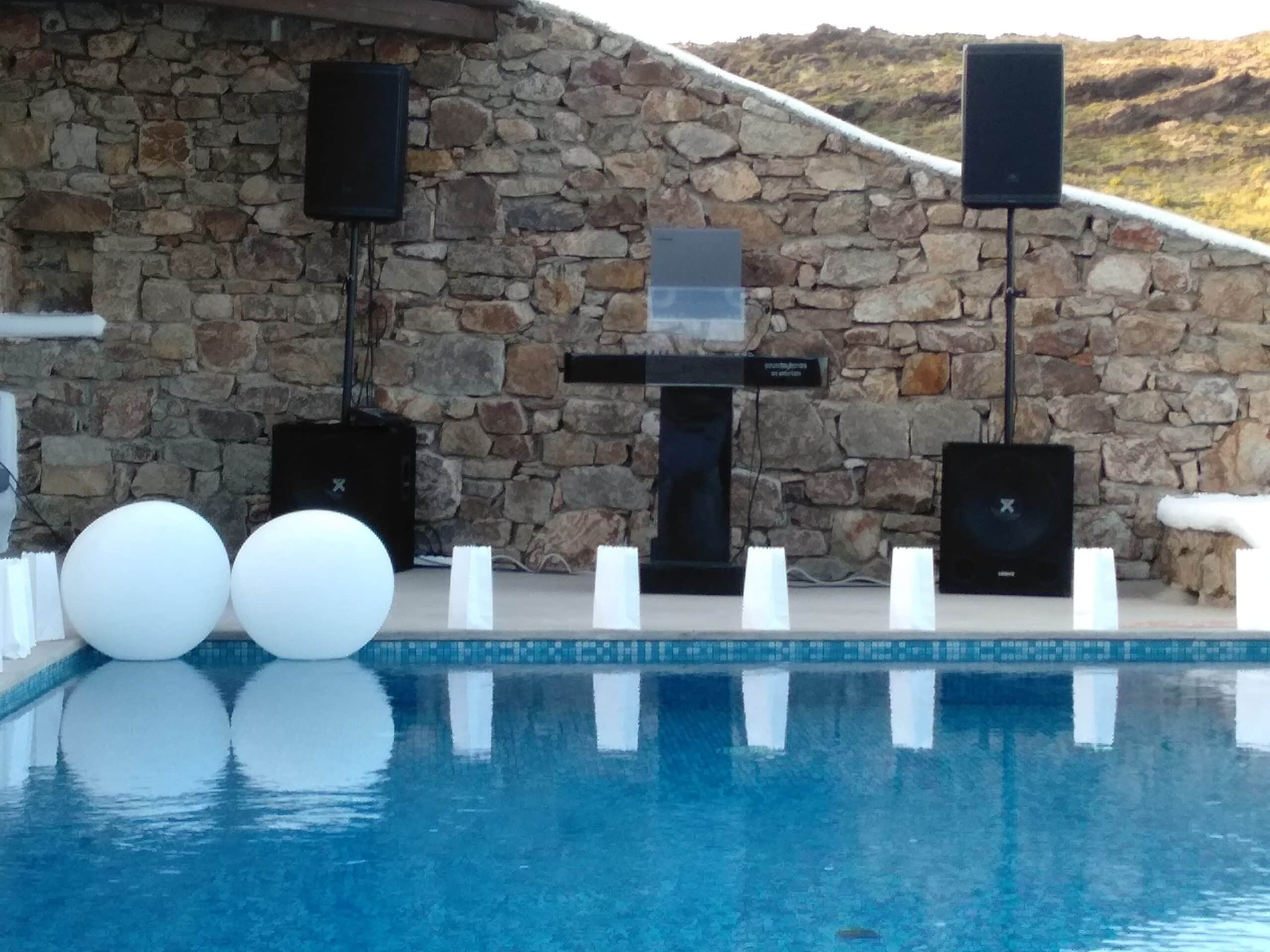 SoundMykonos DJ booth with speakers on stands and subwoofers, set up beside a villa pool