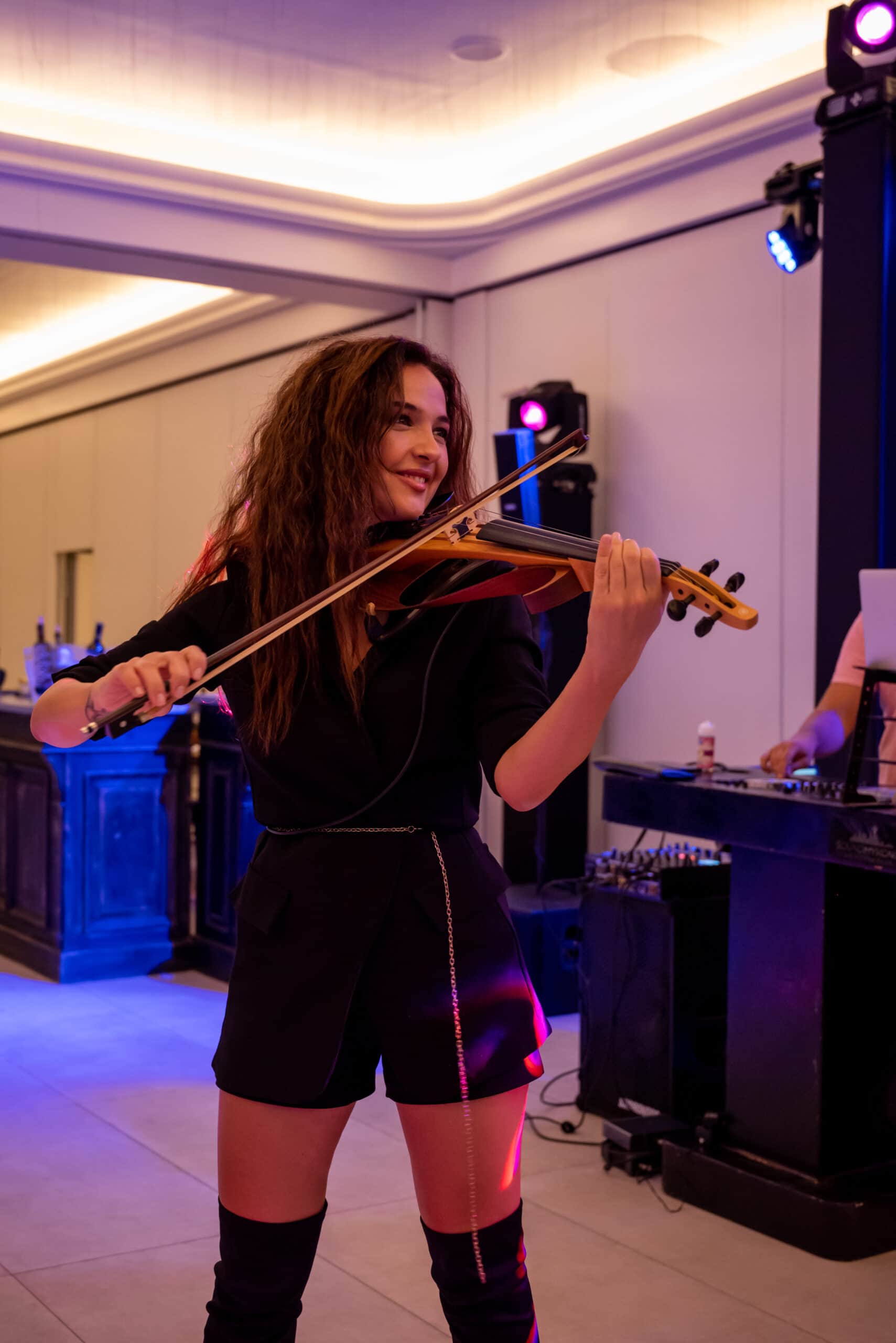Violinist performing in front of the DJ booth under moving-head lights