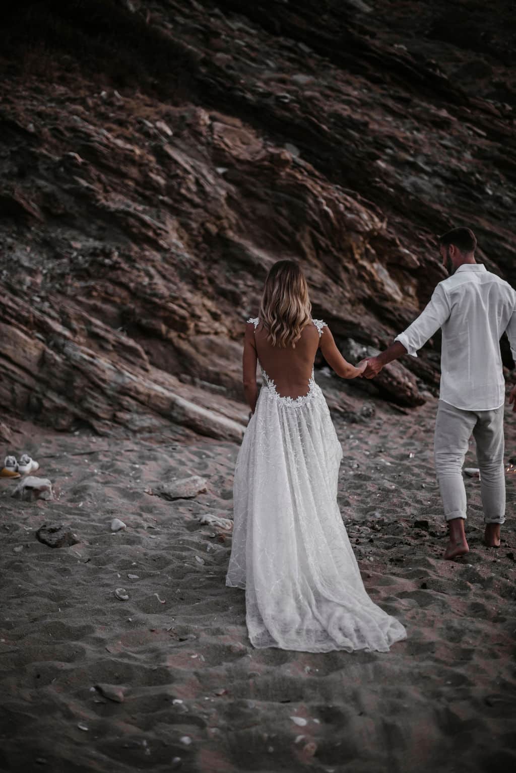 Couple walking hand in hand along a rocky shoreline after a proposal